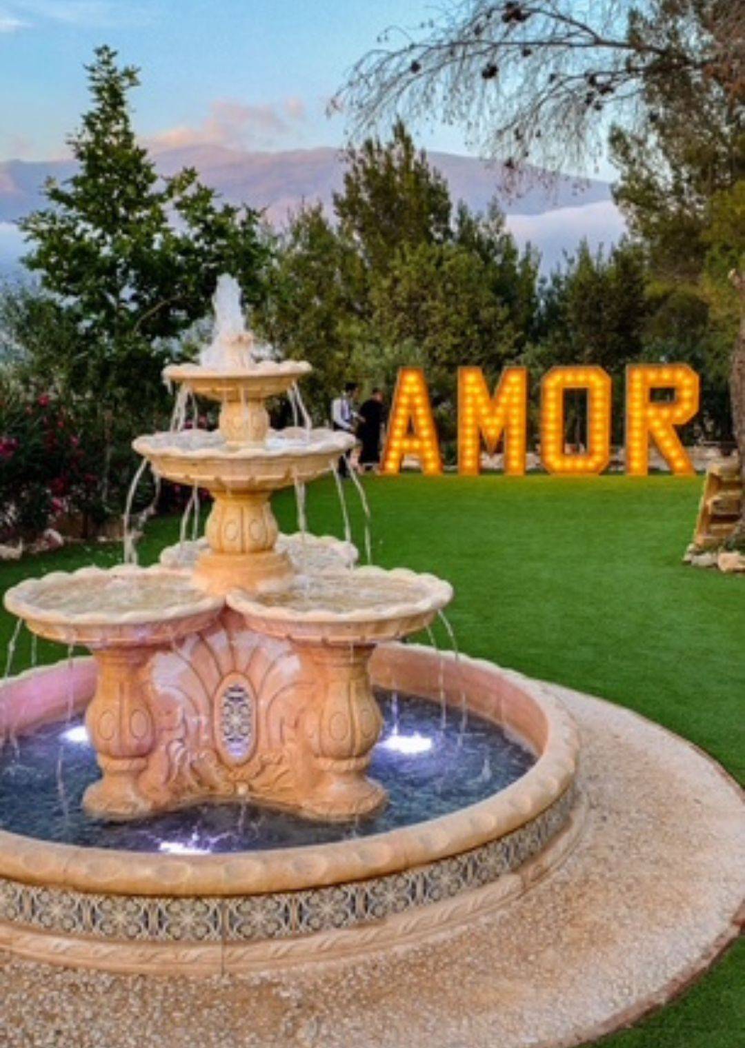 Romantic Wedding Fountain and AMOR Sign at La Esperanza Granada – Luxury Wedding Venue in Spain Romantic wedding decor at La Esperanza Granada, one of the best places to get married in Spain, featuring a tiered Andalusian fountain and illuminated AMOR sign surrounded by lush gardens at sunset.