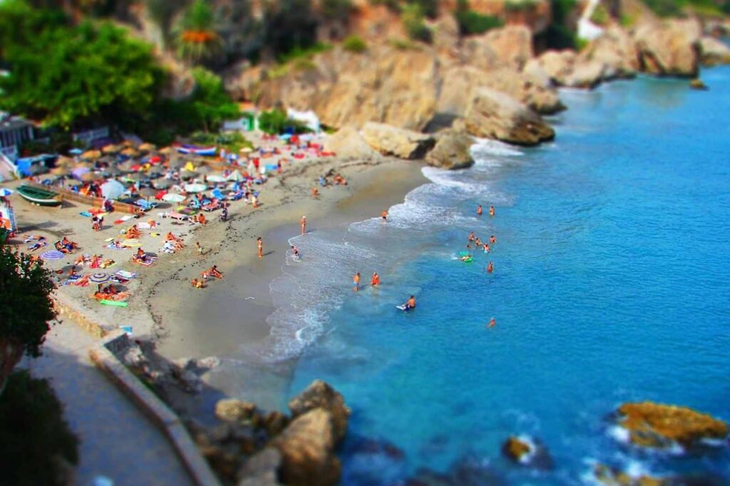 Overhead view of Burriana Beach in Nerja, Andalusia, showing colorful umbrellas, sunbathers, and swimmers enjoying the turquoise Mediterranean waters along Spain’s Costa Tropical — a popular seaside escape near Granada.