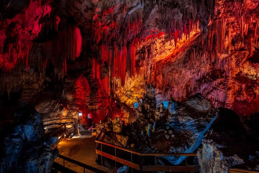 Spectacular view inside the Caves of Nerja in southern Spain, with dramatic red and amber lighting highlighting towering stalactites and stalagmites in the vast underground chambers — one of Andalusia’s most awe-inspiring natural attractions.