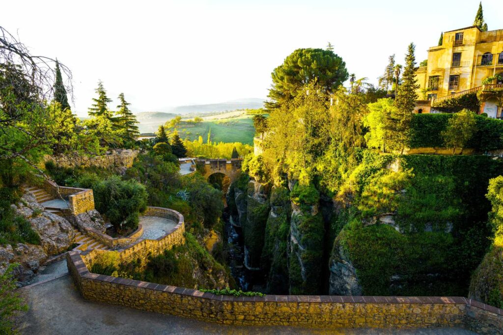Scenic terraced gardens and stone pathways overlooking the deep El Tajo Gorge in Ronda, Andalusia, Spain, surrounded by lush greenery and golden afternoon light — one of the most picturesque viewpoints in southern Spain.