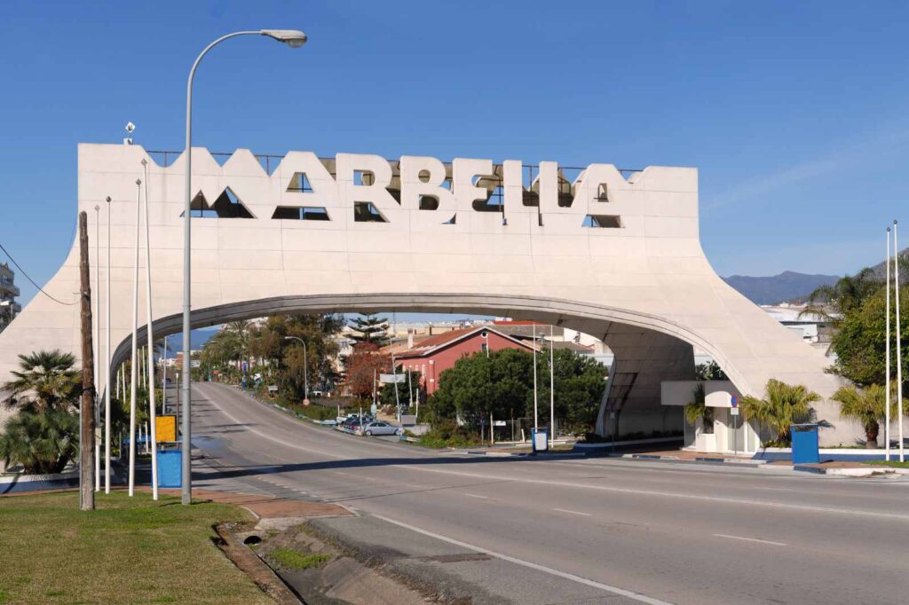 The famous Marbella arch welcoming visitors to the Costa del Sol, with clear blue skies and palm-lined roads leading into the city.