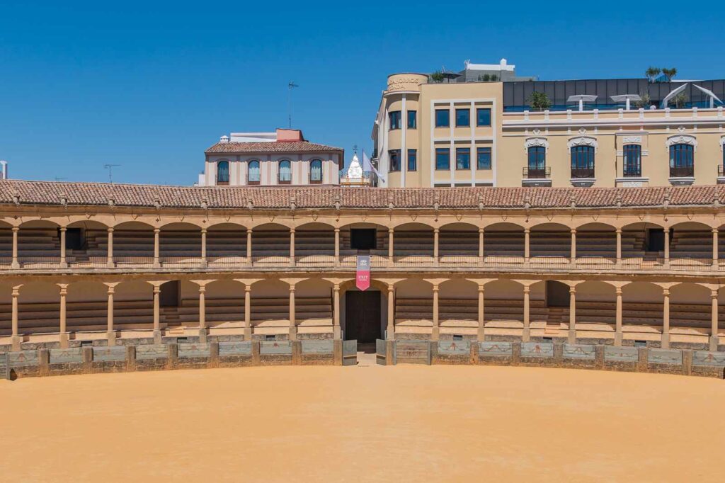 Exterior view of the Plaza de Toros de Ronda in Andalusia, Spain, one of the oldest and most elegant bullrings in the country, featuring traditional arches and golden sand under a bright blue sky.